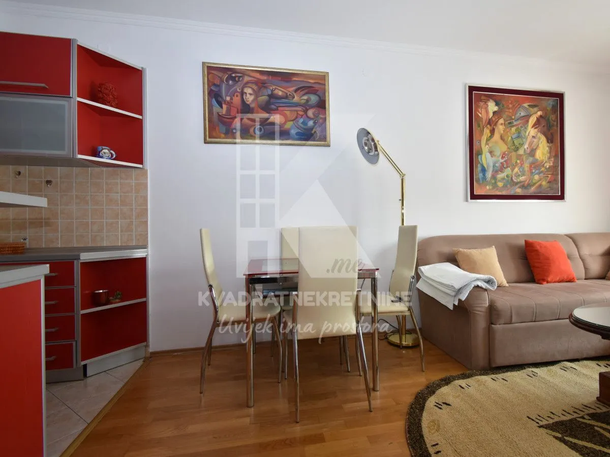 Living room with a dining area and an open kitchen with red units.