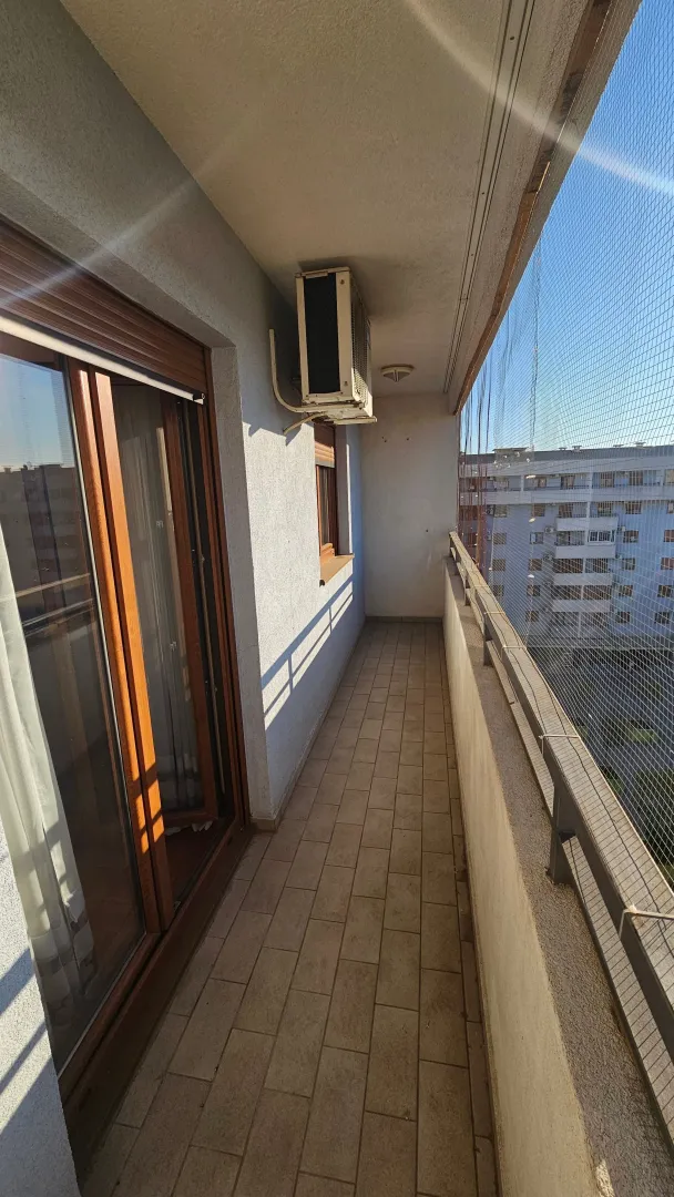 Dugačka popločana terasa sa zaštitnom mrežom i spoljnom jedinicom klima uređaja.