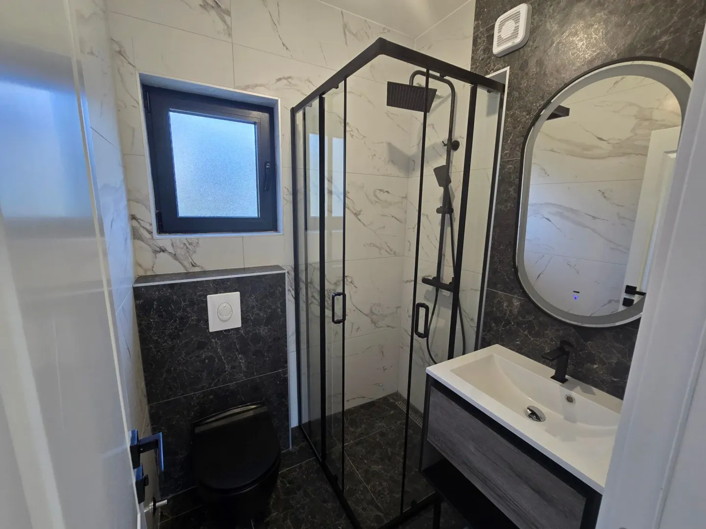 Moderne kupatilo sa tuš kabinom, umivaonikom i crnom toalet šoljom.