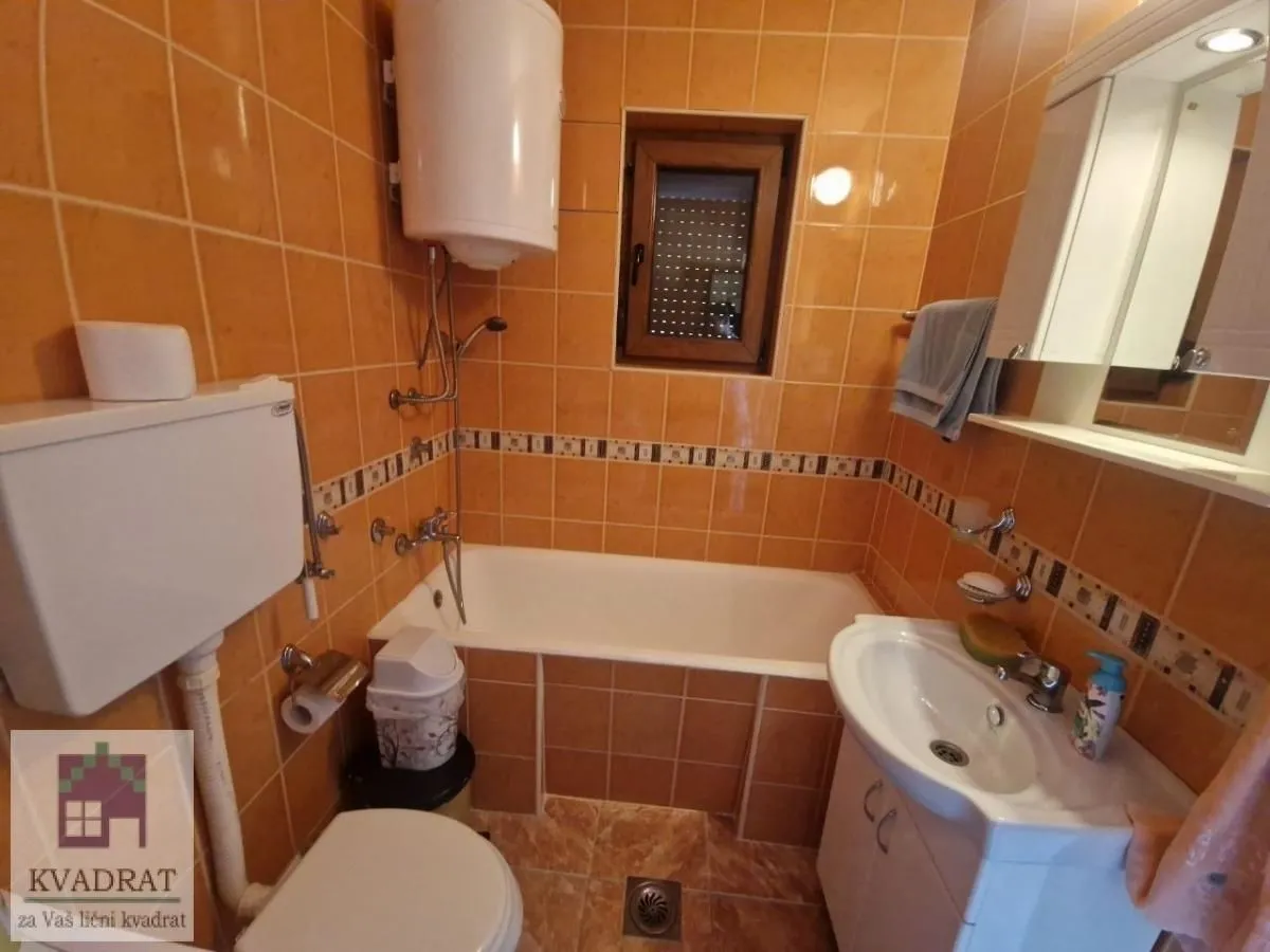 Kupatilo sa kadom, umivaonikom, WC šoljom i pločicama u toplim tonovima.
