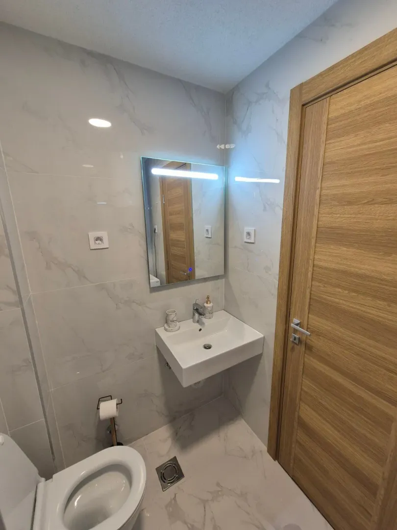 A modern equipped bathroom with a washbasin, mirror, and toilet.