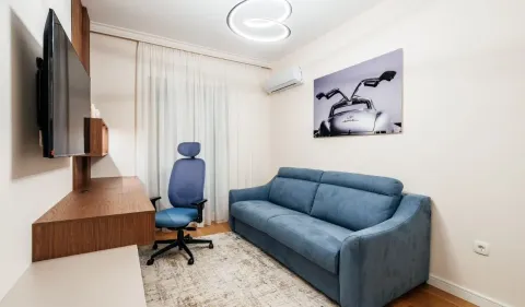 Manja dnevna soba sa plavim trosjedom, radnim stolom i televizorom na zidu. - image 6