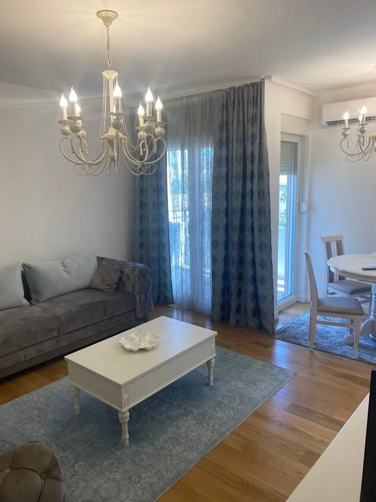 Svijetla dnevna soba sa modernim namještajem, lusterom i trpezarijskim stolom.
