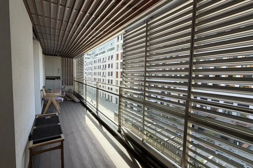 Spacious enclosed balcony with wooden flooring, ceiling paneling, and city views.