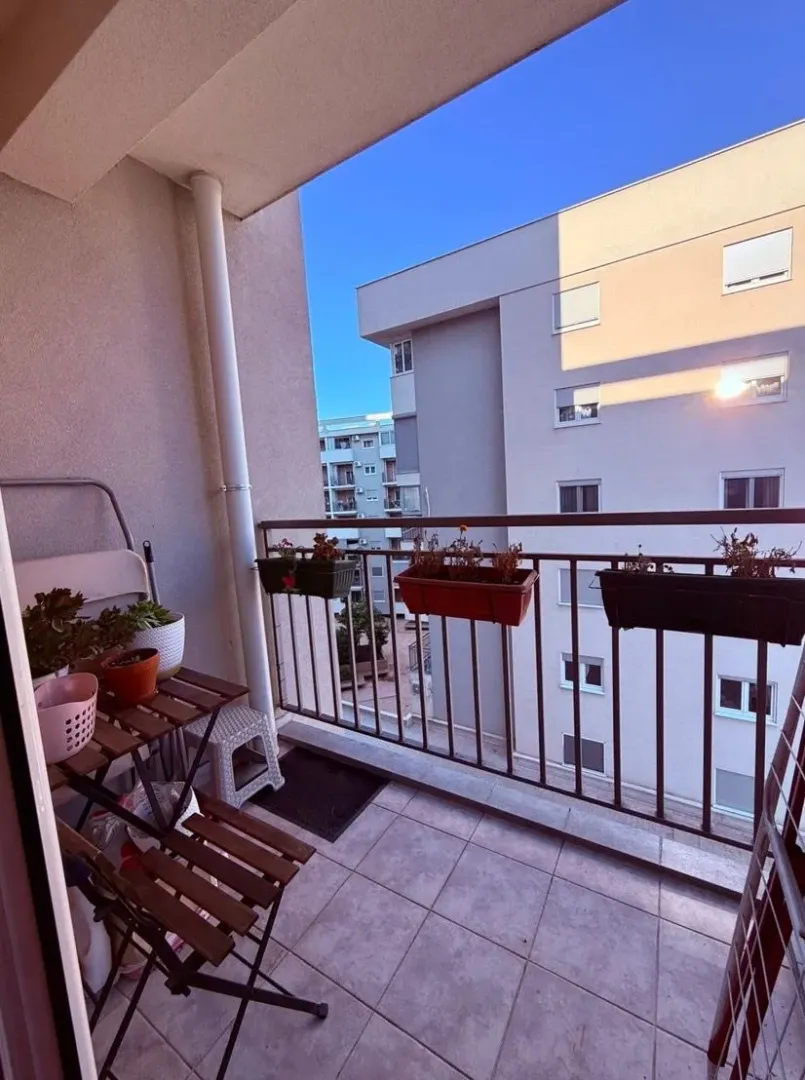 Small furnished balcony with a wooden table and flower planters.