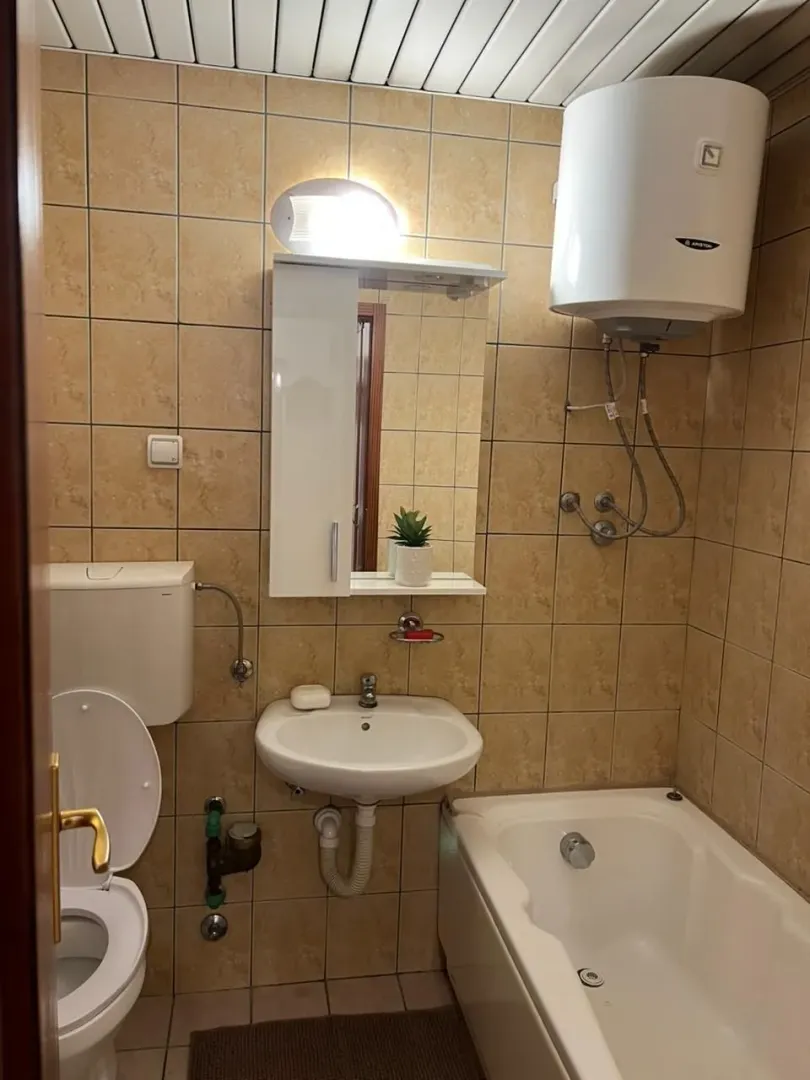 Small tiled bathroom with a bathtub, washbasin, and water heater.