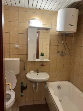 Small tiled bathroom with a bathtub, washbasin, and water heater. - image 8