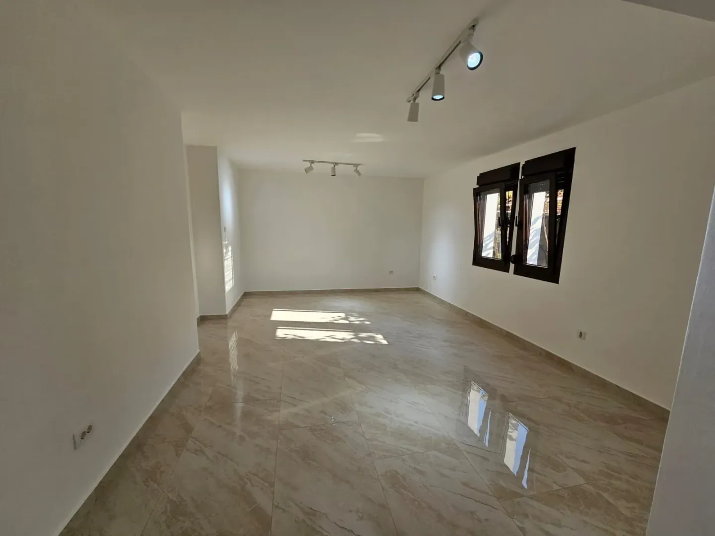 An empty room featuring light-colored tiled flooring, white walls, and track lighting.