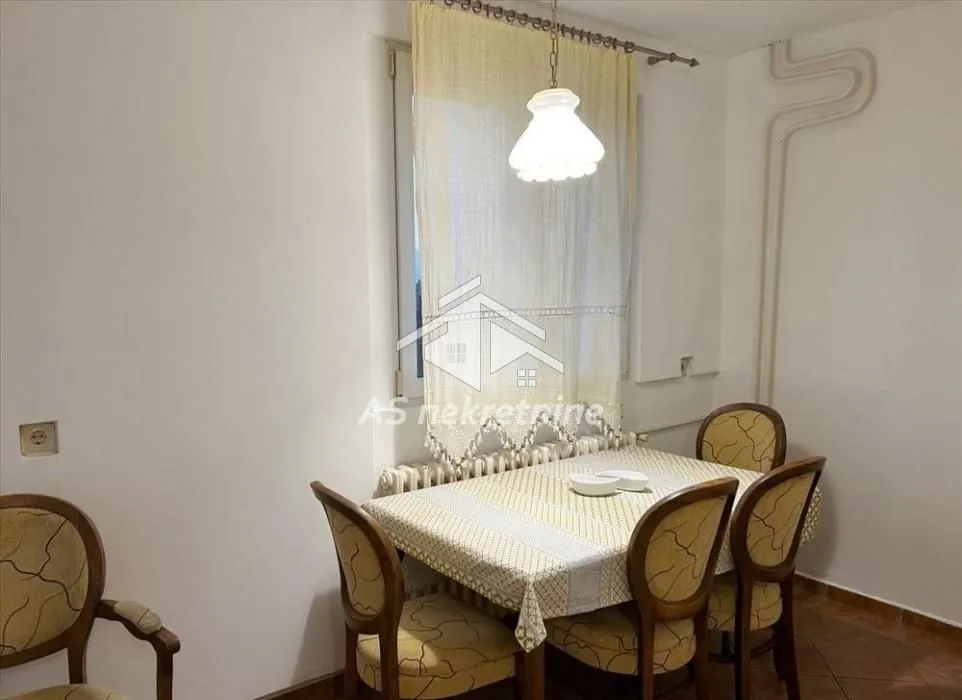 Dining area with a table, chairs, and a chandelier near the window.