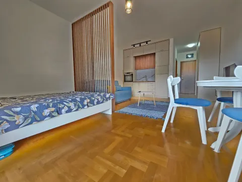 View of the living room with a bed, wooden partition, and kitchen in the background. - image 12