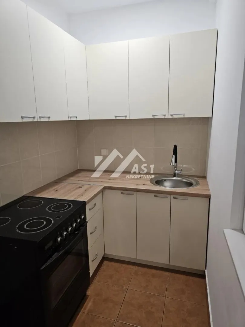 Manja opremljena kuhinja sa belim elementima i šporetom.