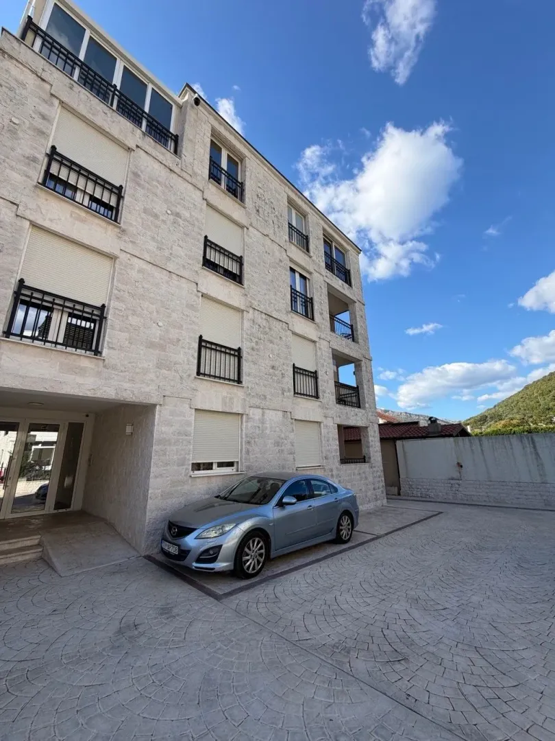 Eksterijer višestambene zgrade sa popločanim dvorištem i parking prostorom.