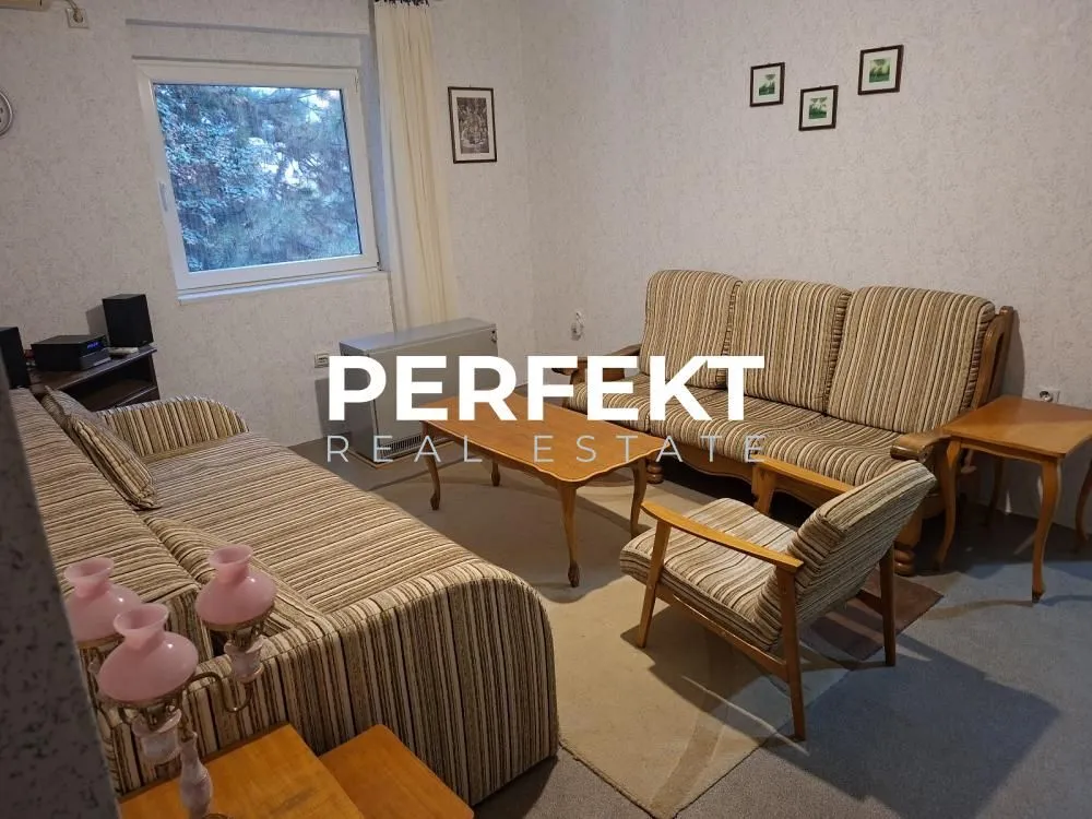 Dnevna soba sa garniturom za sedenje, foteljom, stočićem i prozorom.