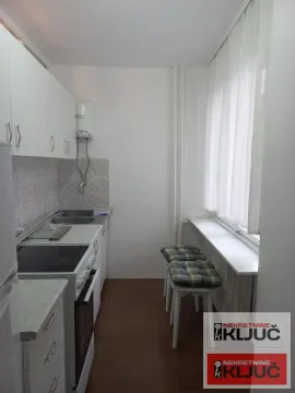 Manja kuhinja sa belim elementima i šankom sa stolicama pored prozora. - image 6