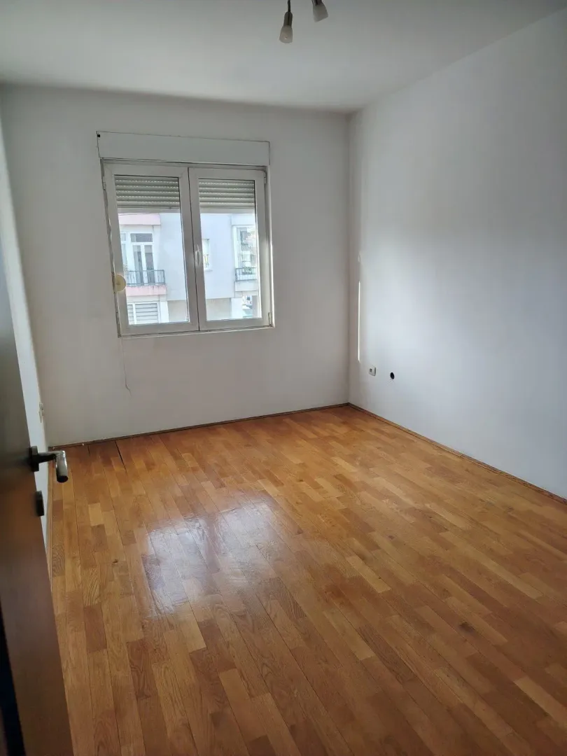Prazna soba sa parketom i prozorom.