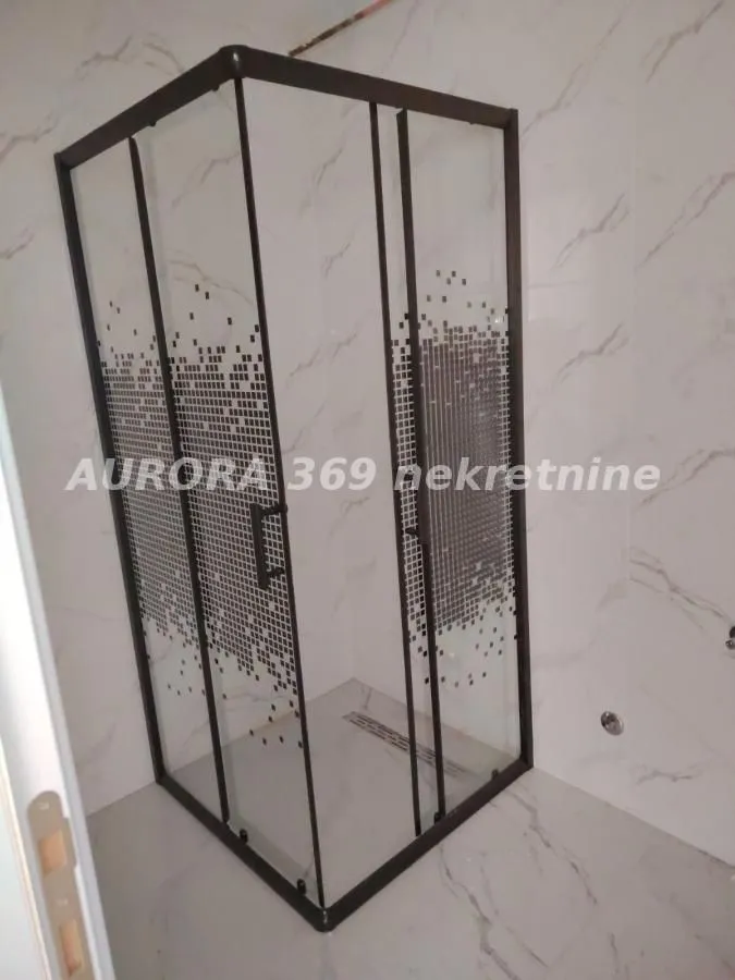 Tuš kabina sa staklenim paravanom i keramičkim pločicama na zidu.