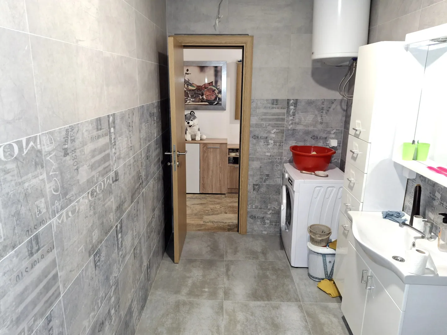 Moderne kupatilo sa sivim pločicama, veš mašinom i bijelim sanitarijama.