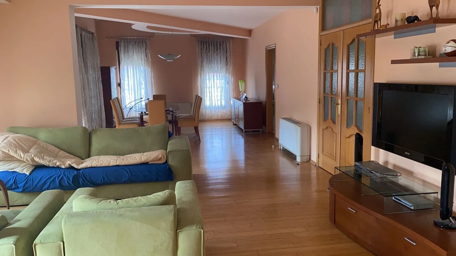 Dnevna soba sa zelenom garniturom, televizorom i trpezarijskim stolom u pozadini.