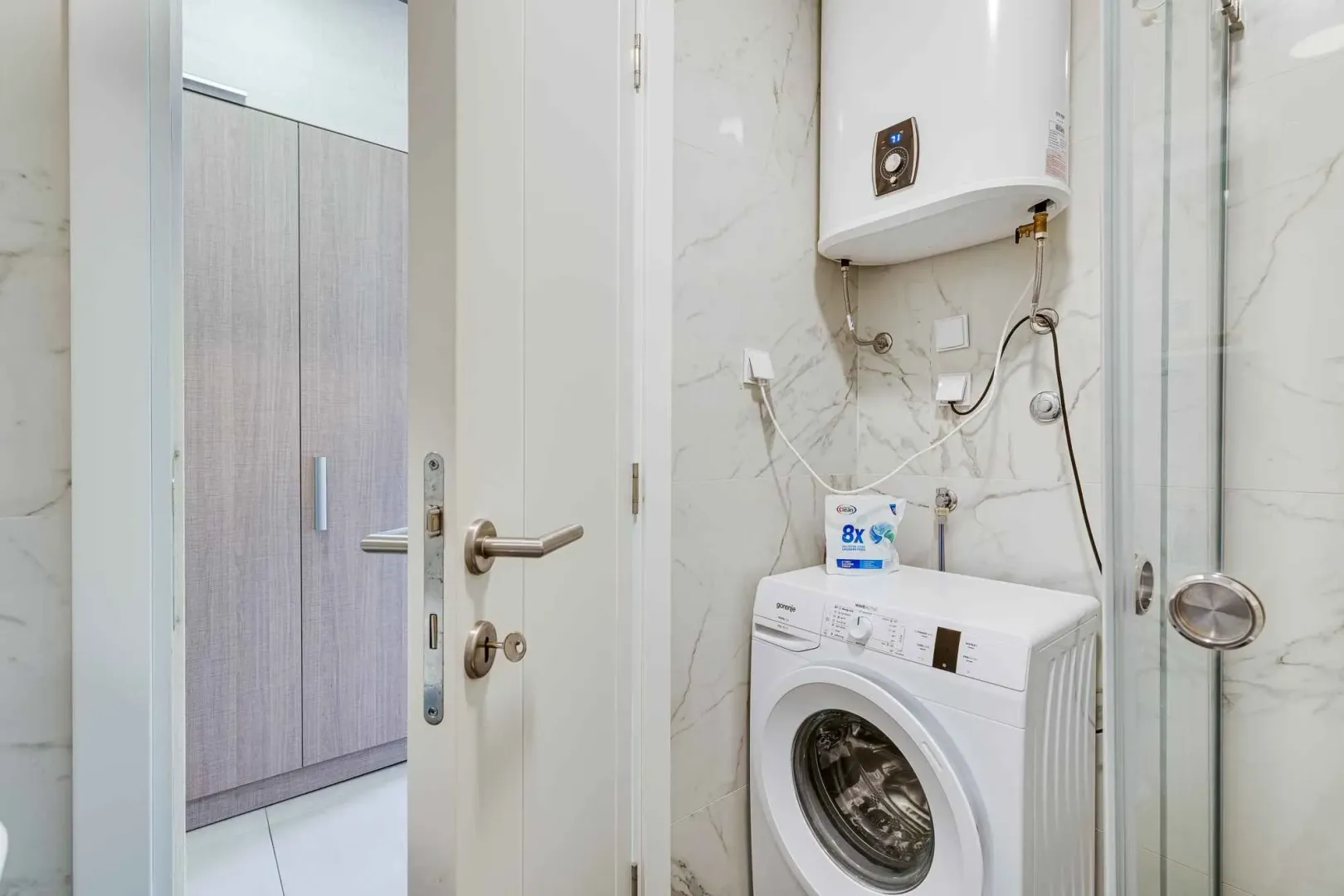 Small bathroom with a washing machine, water heater, and shower cabin.