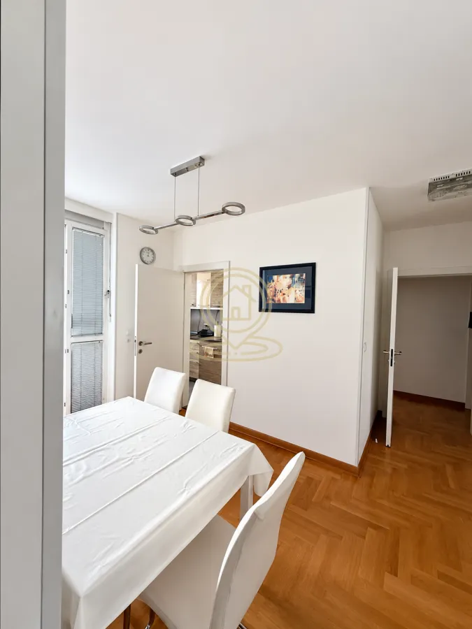Dining area with a table, white chairs and a view of the kitchen in the background.