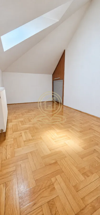 Prazna soba sa kosim krovom, parketom i krovnim prozorom.