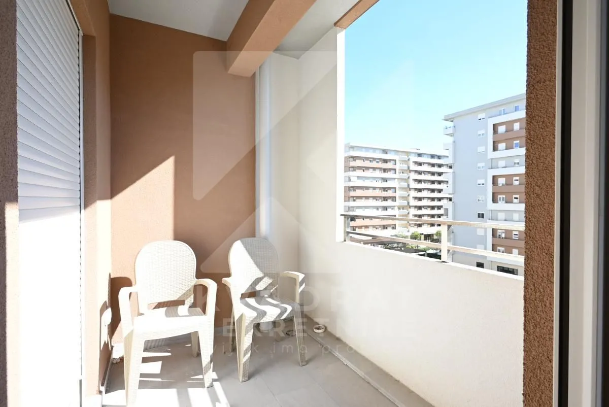 Covered balcony with two white chairs and a view of surrounding buildings.