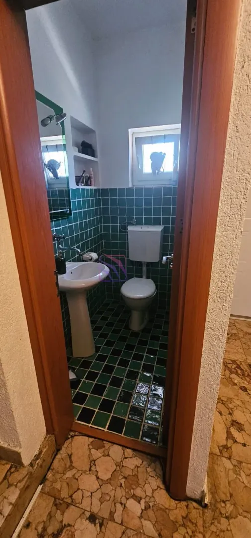 Pogled iz hodnika na manje kupatilo sa zelenim pločicama.