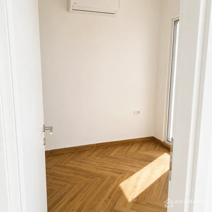 Pogled iz hodnika na manju sobu sa parketom i klima uređajem.