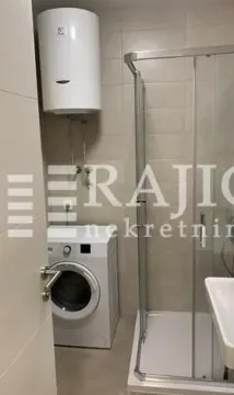 Small bathroom with a shower cabin, water heater, and washing machine. - image 7
