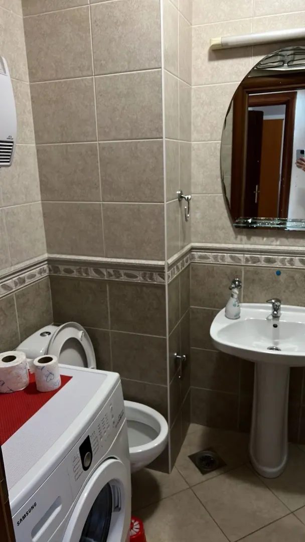 Kupatilo sa pločicama, lavaboom, ogledalom i veš mašinom.