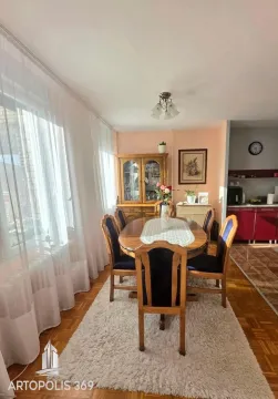 Trpezarija sa drvenim stolom, stolicama i vitrinom, povezana sa kuhinjom. - image 3