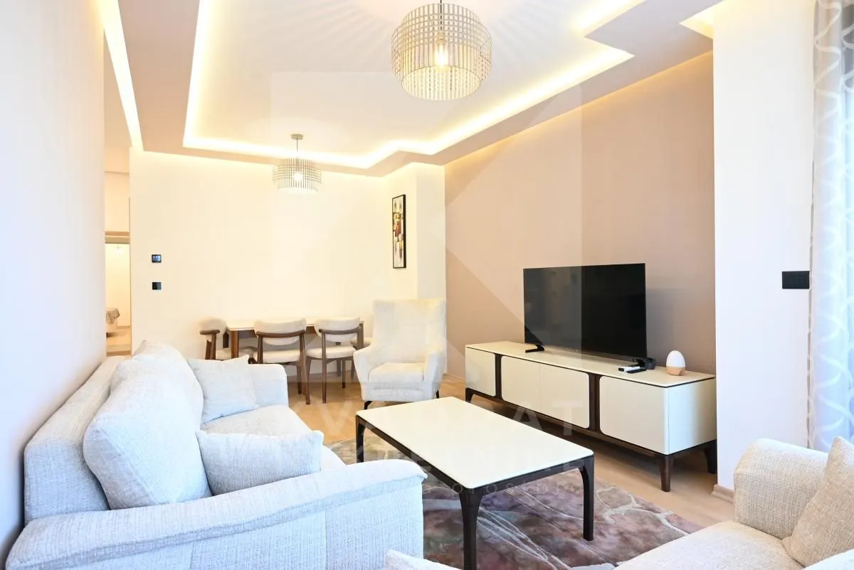 Spacious living room with sofa, television and dining area in the background.