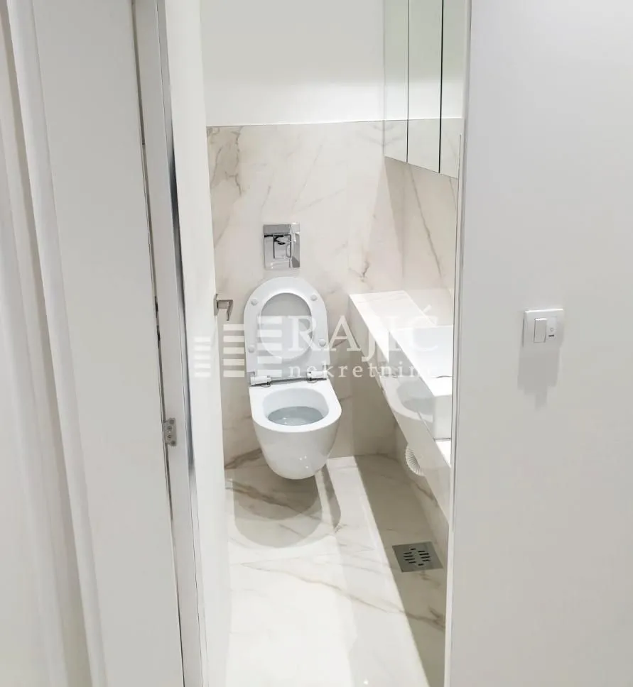 View of a modernly equipped bathroom with white sanitary ware and marble tiles.
