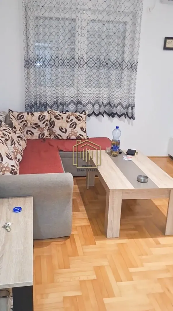Dnevna soba sa garniturom, stočićem i parketom na podu.