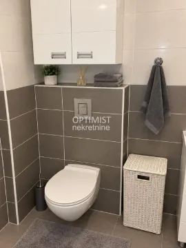 Pogled na kupatilo sa klozetskom šoljom, belim ormarićem i pletenom korpom za veš. - image 15