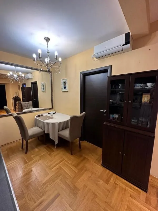 Trpezarija sa stolom, stolicama, velikim ogledalom i tamnim drvenim ormarom.