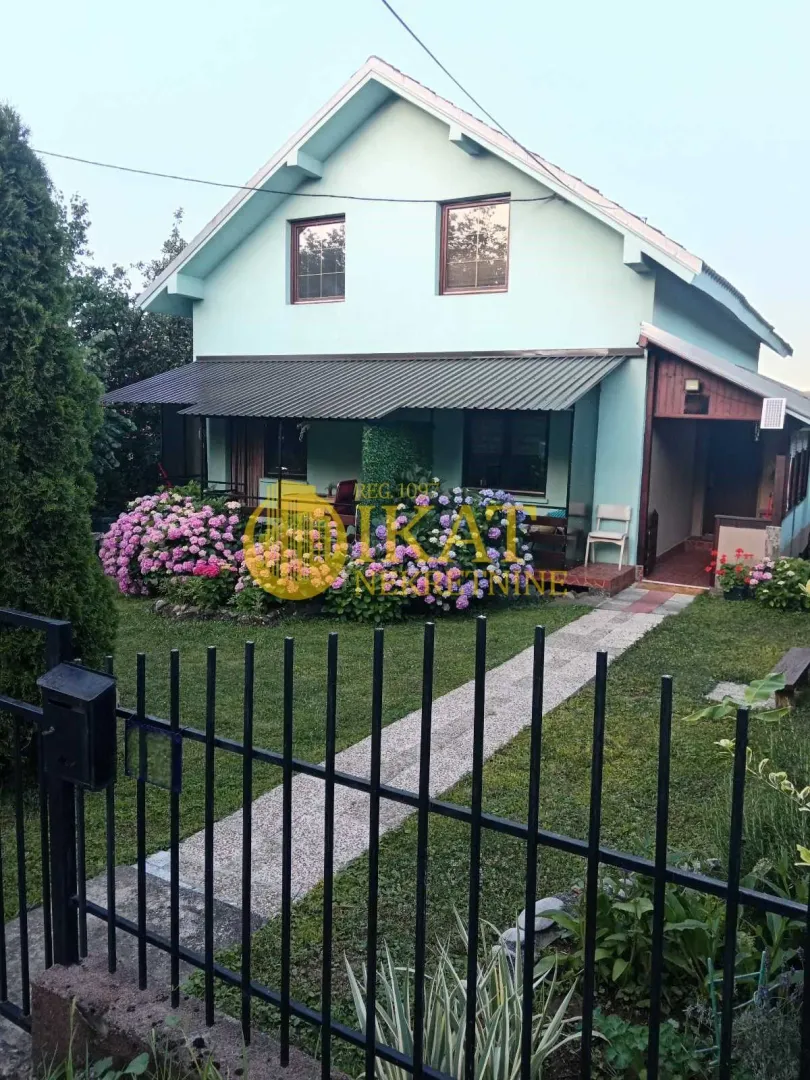 Pogled na prednju stranu kuće sa uređenim dvorištem i cvećem.