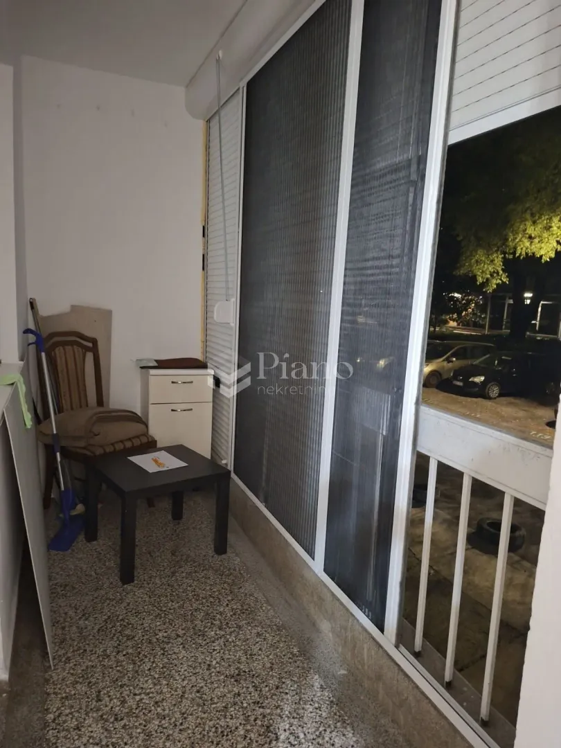 Small enclosed balcony with glass sliding doors and a small piece of furniture.
