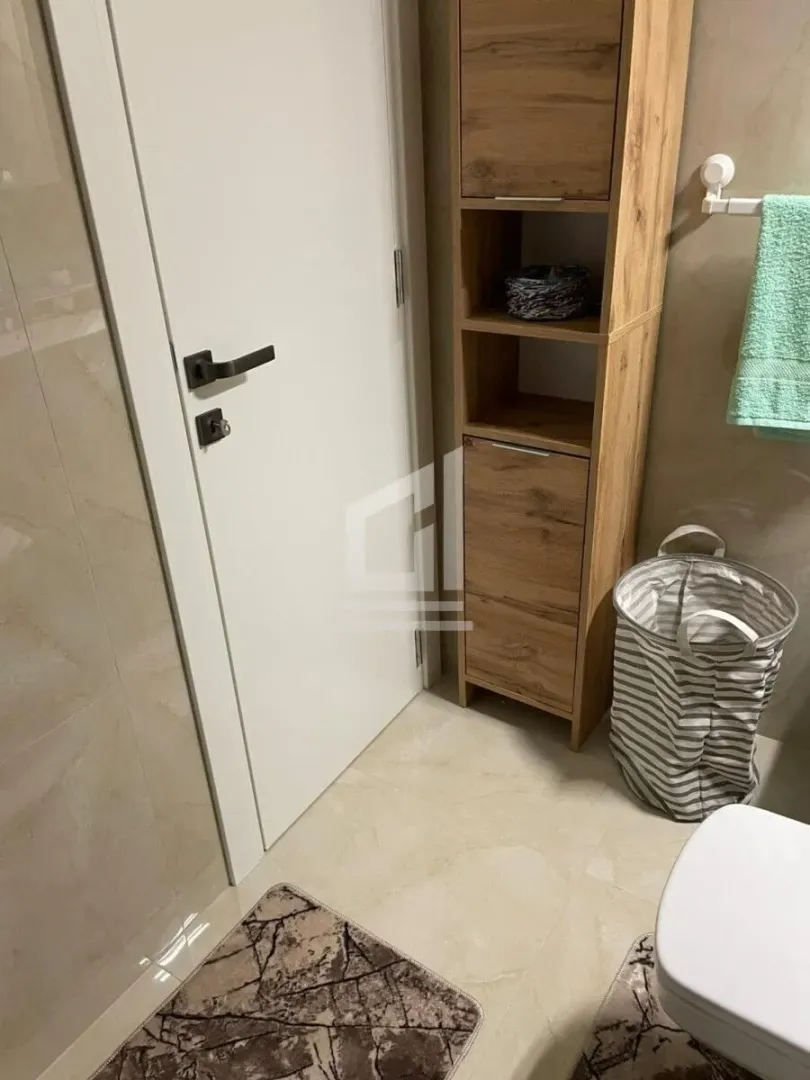 View of the bathroom with a wooden cabinet, laundry basket, and door.