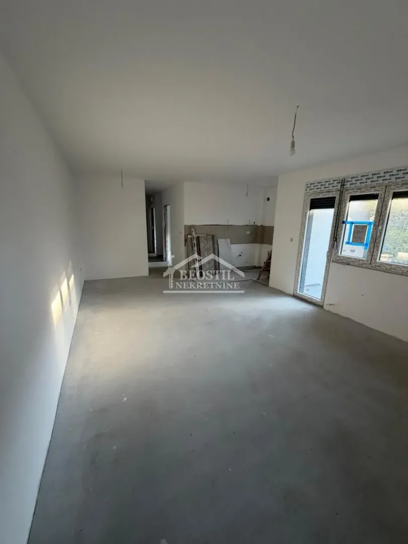 Nenameštena prostorija u izgradnji sa belim zidovima i betonskim podom.