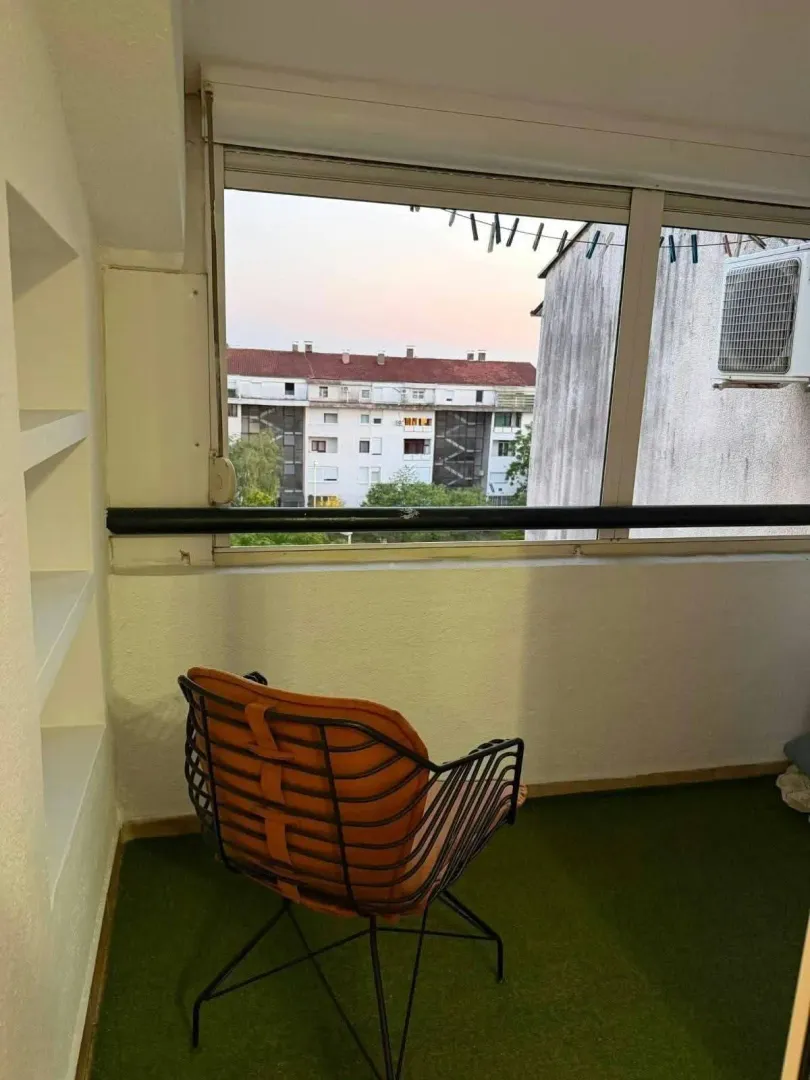 Zastakljena terasa sa foteljom i pogledom na naselje.