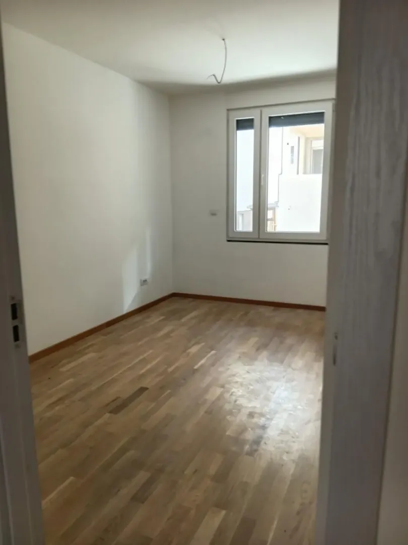 Prazna soba sa parketom i belim zidovima.
