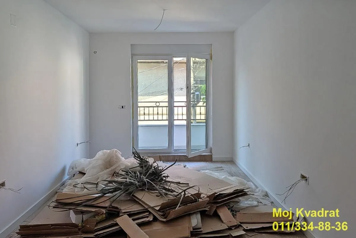 Prazna prostorija u toku renoviranja sa gomilom kartona i materijala na podu.