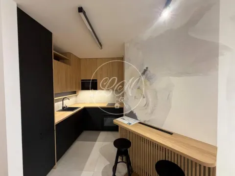 Modern kitchen with dark cabinetry and a wooden breakfast bar with bar stools. - image 7