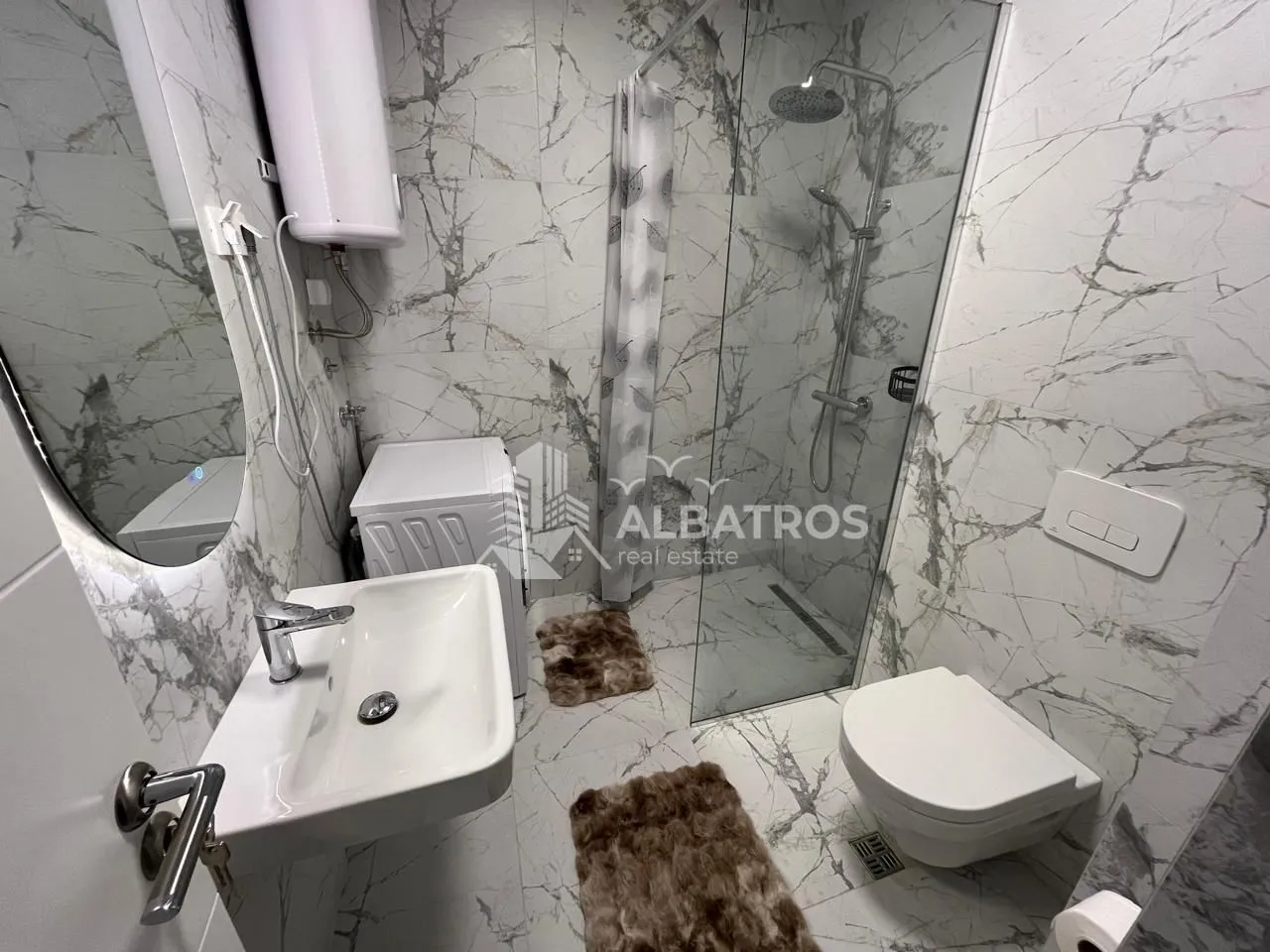 Modern bathroom with a walk-in shower, washbasin, and toilet, finished with marble tiles.