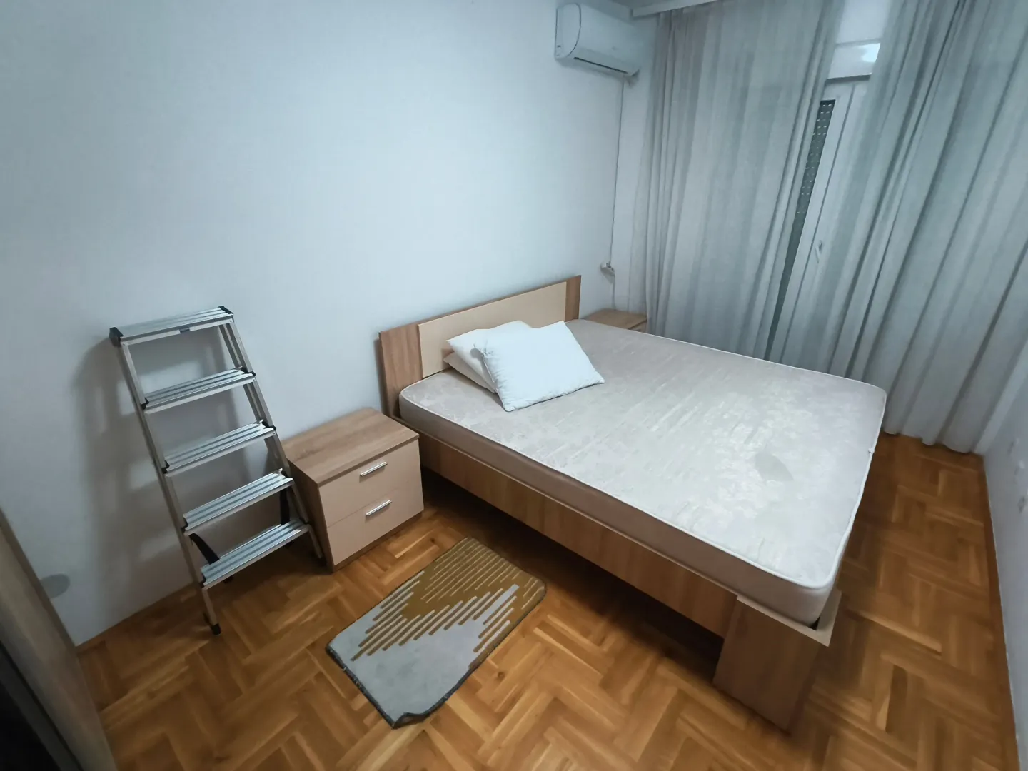 Spavaća soba sa bračnim krevetom, noćnim stočićima i klima uređajem.