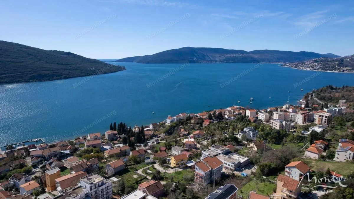 Pogled iz vazduha na zaliv i primorsko naselje sa brdima u pozadini.