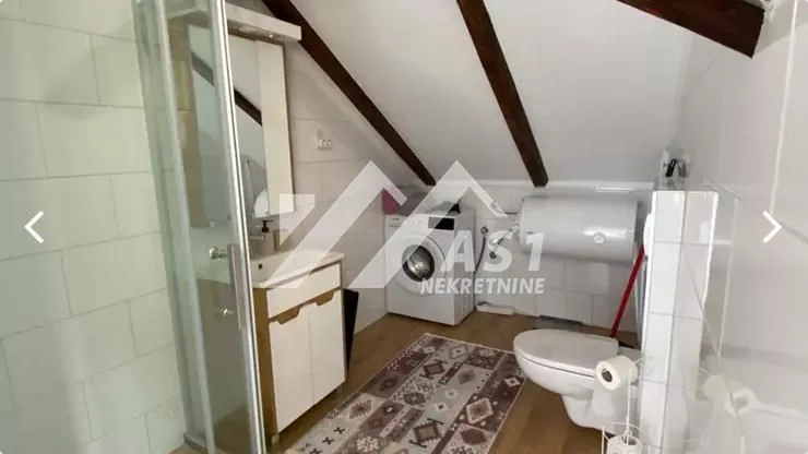 Kupatilo u potkrovlju sa tuš kabinom, umivaonikom, veš mašinom i WC šoljom.