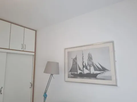 White wall with a built-in wardrobe, floor lamp, and a framed picture of a sailing ship. - image 12