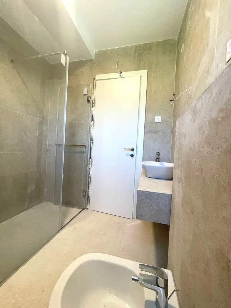 Bathroom with a walk-in shower, washbasin, and installed sanitary fixtures.